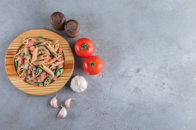 Lekkere penne pasta met verse gehakte groenten op houten plaat.