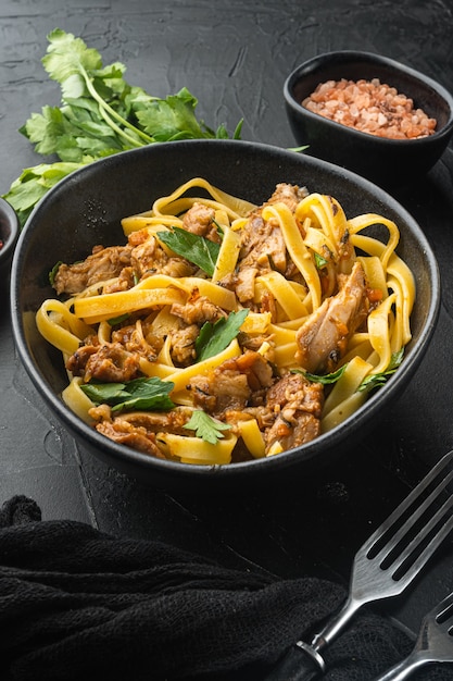 Lekkere pittige konijnenstoofpot met pasta tagliatelle of pappardelle set, in kom, op zwarte stenen tafel