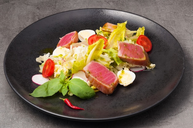 Lekkere salade met gebakken tonijn, groenten en kwarteleitje op een zwarte plaat