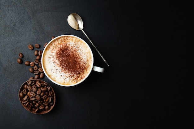 Lekkere smakelijke cappuccino in beker met bonen op donkere tafel.