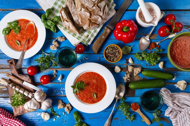 Lekkere smakelijke klassieke Spaanse soep gazpacho in witte borden op rustieke blauwe tafel met brood, knoflook en specerijen. Diner Concept. Bovenaanzicht.