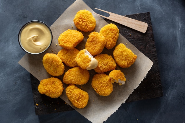 Lekkere smakelijke knapperige kipnuggets geserveerd op een houten bord met mosterd op donkere ondergrond.