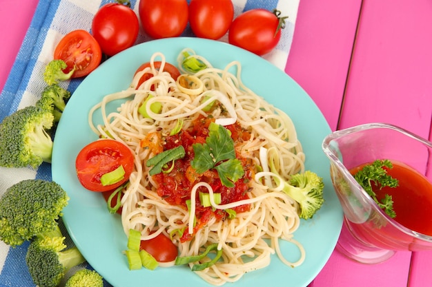 Lekkere spaghetti met saus en groenten op plaat op houten tafel close-up