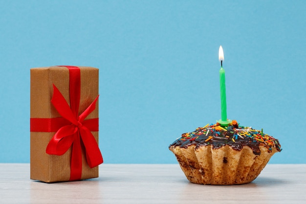 Lekkere verjaardag cupcake met chocolade glazuur en karamel, versierd met brandende feestelijke kaars en geschenkdoos op blauwe achtergrond. Gelukkige verjaardag minimaal concept.