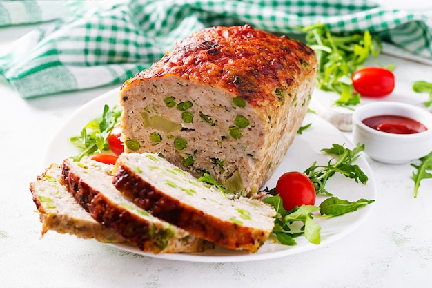 Lekkere zelfgemaakte gemalen gebakken kippengehaktbrood met groene erwten en gesneden broccoli op witte tafel