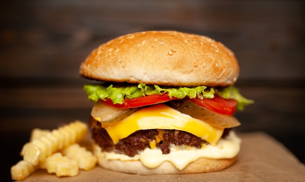 Lekkere zelfgemaakte hamburger met rundvlees, sla, kaas, komkommer en frietjes op een houten achtergrond