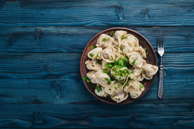 Lekkere zelfgemaakte vlees dumplings van volkoren meel of Russische pelmeni besprenkeld met verse peterselie op plaat op houten tafelkopie ruimte weergave van bovenaf