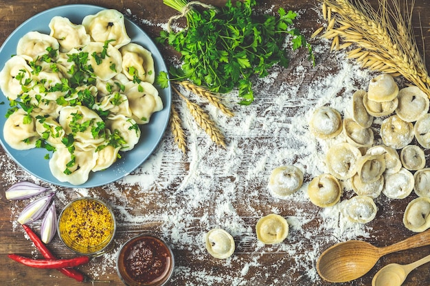 Lekkere zelfgemaakte vleesknoedels of traditionele Italiaanse ravioli van volkorenmeel bestrooid met verse peterselie op bord en rauwe ravioli op donker houten tafeloppervlak kopie ruimte van bovenaf bekijken