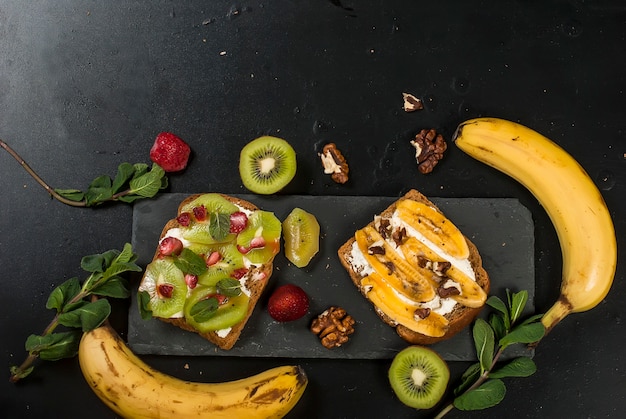 Lekkere zoete broodjes met bananen, noten en chocolade, kiwi, aardbeien en mint op zwarte achtergrond