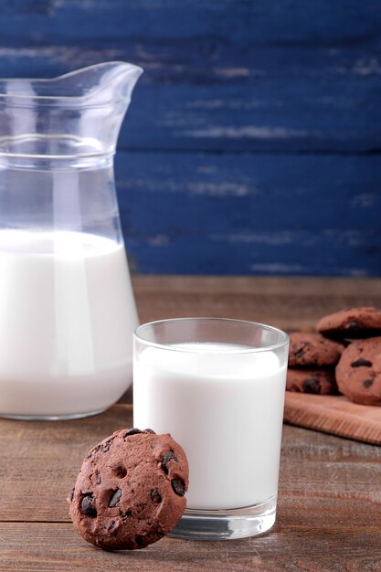 Lekkere zoete koekjes met chocolade en melk op een bruin houten tafel en op een blauwe achtergrond