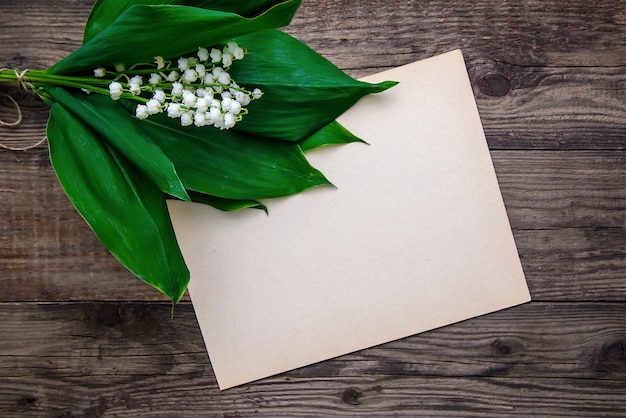 Lelietje-van-dalenboeket en een vel papier op een houten ondergrond