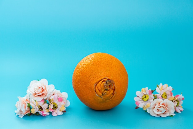Lelijke sinaasappel en bloemen op een blauwe achtergrond. het concept van zorg en preventie van proctologische ziekten.