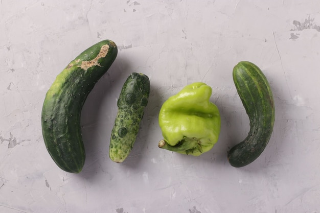 Lelijke verse komkommers en peper op lichtgrijze achtergrond. Concept biologische natuurlijke groenten. Uitzicht van boven