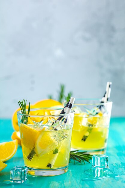 Lemon alcohol drink cocktail with ice lemon and rosemary herb on a blue turquoise wooden table background surface Traditional italian homemade lemon alcohol drink liqueur limoncello