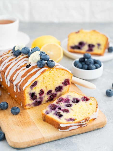 Lemon blueberry cake with lemon icing and fresh berries on top on the board on a gray background