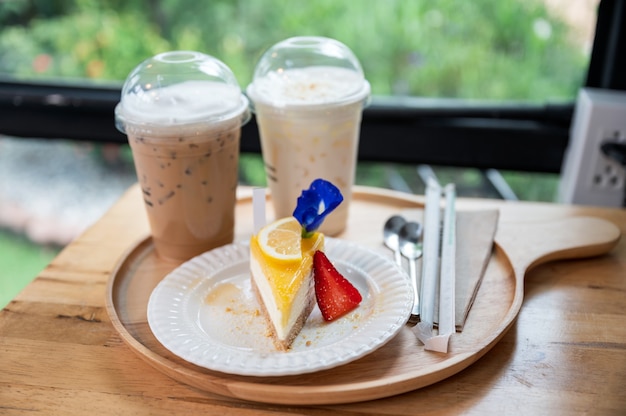 Lemon cake with biscuit and ice coffee on wooden tray in cafe