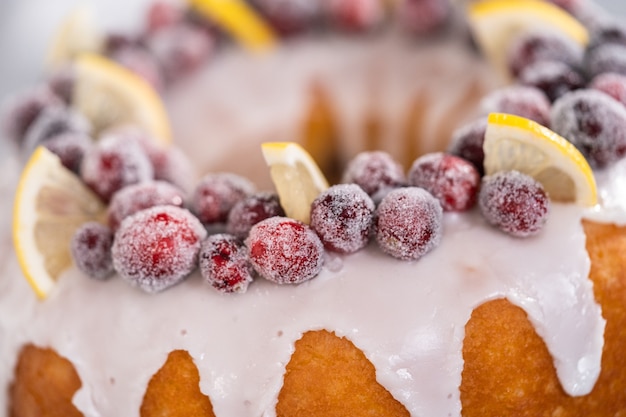 Lemon cranberry bundt cake decorated with sugar cranberries and lemon wedges on a cake stand.