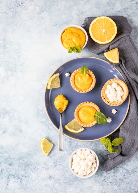 Lemon curd mini tarts decorated with mint and lemon slices on blue ceramic plate. Top view.