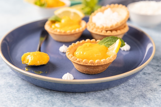 Lemon curd mini tarts decorated with mint and lemon slices on blue ceramic plate.