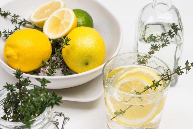 Lemon drink in glass. Thyme sprigs in glass. Lemons on table and in ceramic bowl. Close up.. Top view.
