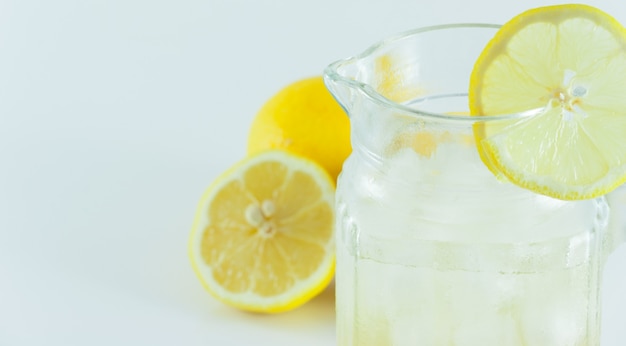 Succo di limone con ghiaccio in una brocca di vetro decorato con fette di limone con cubetti di limone tagliati a metà su uno sfondo bianco