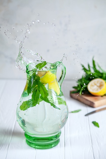 レモンは投手や瓶に水しぶきを作ります。水、レモン、ミントの瓶に天然レモネードのスプラッシュ。さわやかな冷たい飲み物。健康、デトックスの概念。水しぶきが付いているガラス瓶。動きの概念の食品