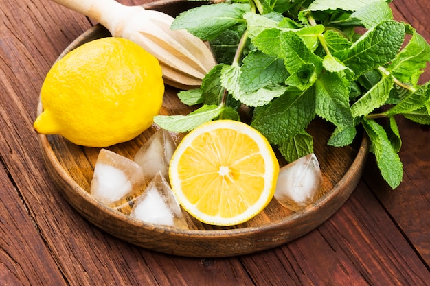 lemon, mint, ice in wooden tray on a wooden background