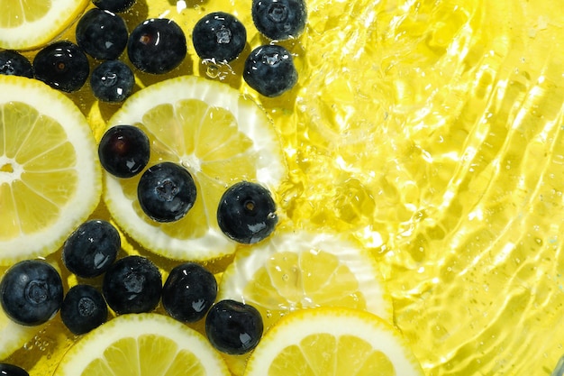 Lemon slices and blueberry in water on yellow background