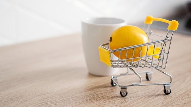 Limone in un piccolo carrello della spesa sul tavolo della cucina. nelle vicinanze c'è una tazza di tè bianco. sfondo cucina leggera e moderna.