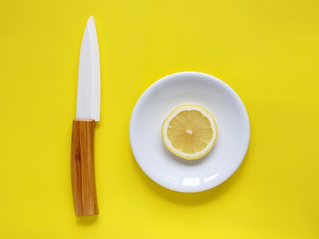 Lemon on a white plate and knife on a yellow background