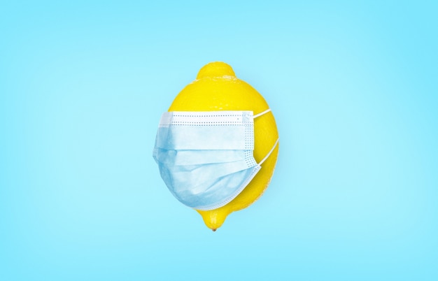 Lemon with a medical mask on a blue background. Vitamins for colds. Coronavirus protection concept. Infection and prevention