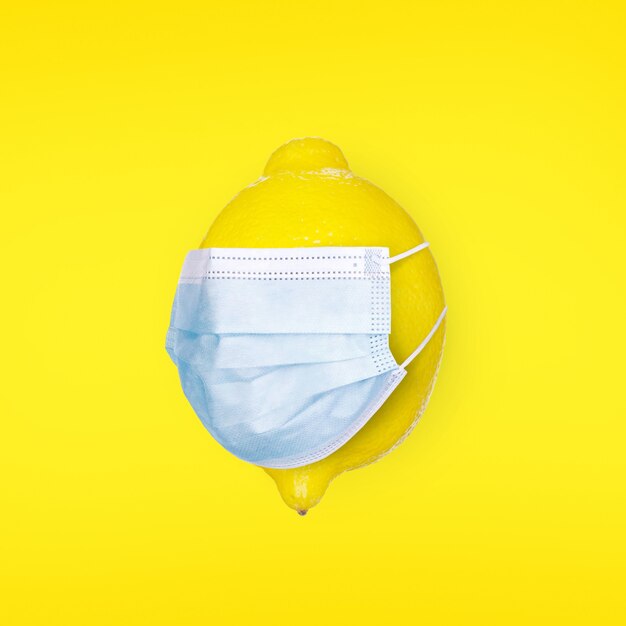 Lemon with a medical mask on a yellow background. Concept of protection and prevention of the virus and disease. Coronavirus, COVID-19, Corona virus concept. Vitamins and Flu Prevention