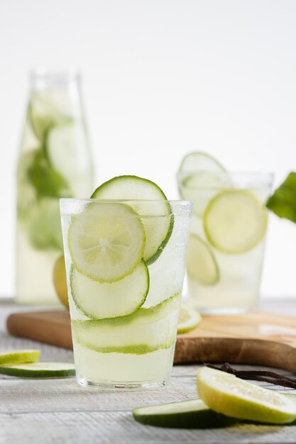 Lemonade bottle and a glass served with lemon and cucumber slices on a light background Copy space