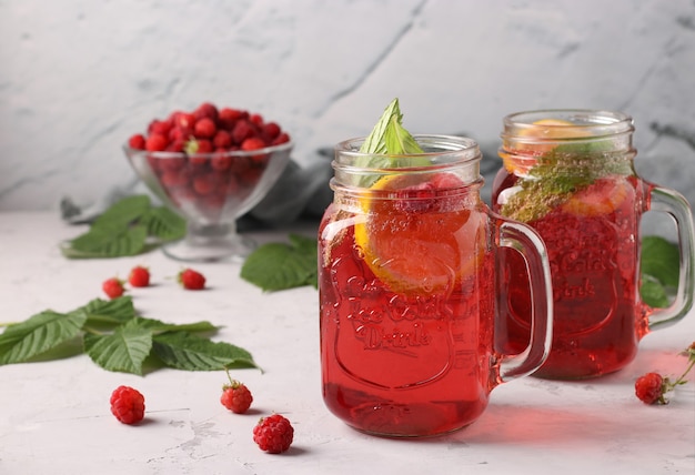 Lemonade or cocktail with raspberries, mint, lemon and ice on a light gray background. Horizontal format