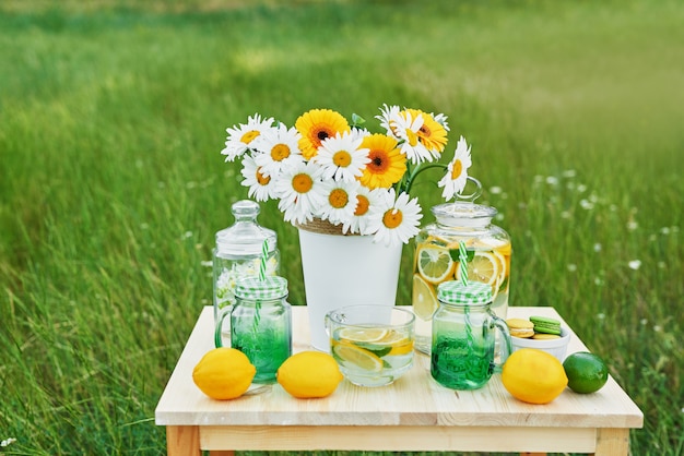 テーブルの上のレモネードとデイジーの花。レモンとレモネードのメイソンジャーガラス。屋外のピクニック。