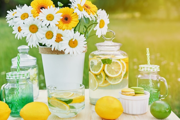 Lemonade and daisy flowers on table. Mason jar glass of lemonade with lemons. Outdoor picnic.