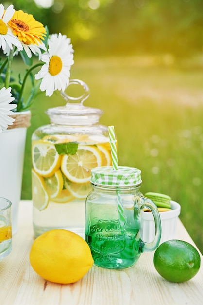 Foto limonata e fiori margherita sul tavolo. barattolo di vetro bicchiere di limonata con limoni. picnic all'aperto.