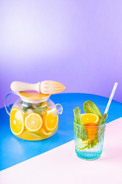 Lemonade drink of water, lemon, orange and mint leaves on multicolored background