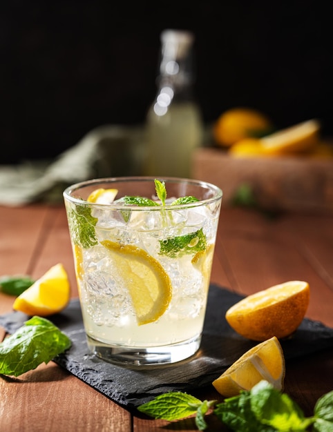 Lemonade drink with fresh lemons Refreshing cocktails with lemon mint and ice on dark wooden background Summer cold drinks concept