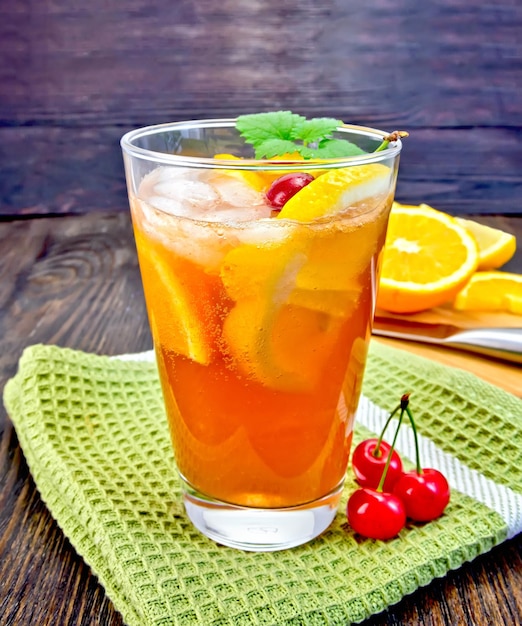 Lemonade in a glass with a cherry lemon and orange mint on green napkin on a dark wooden board