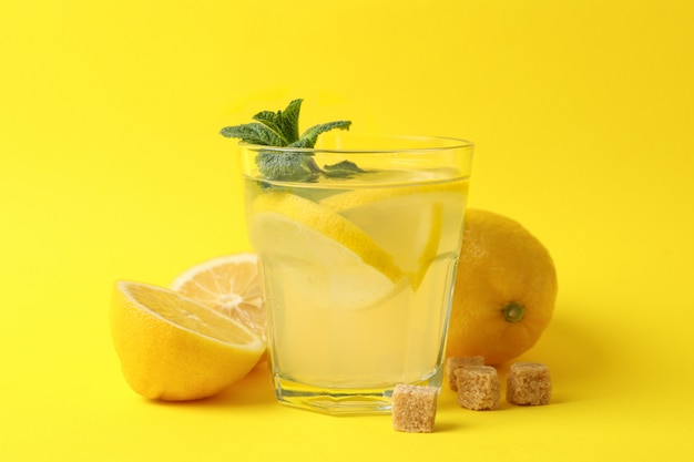 Lemonade, lemons and sugar cubes on yellow surface, close up