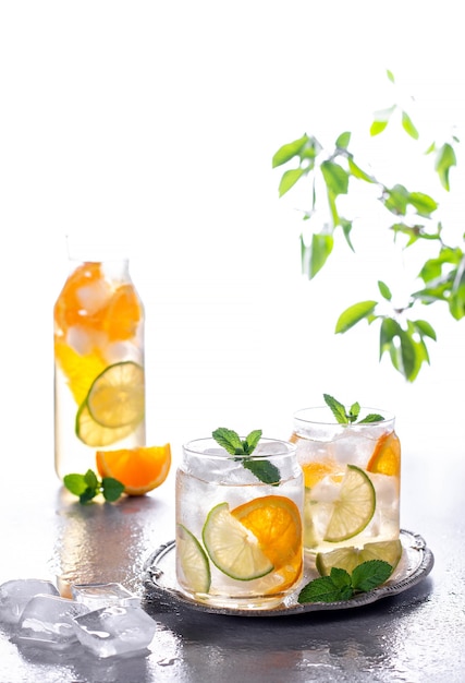 Lemonade or mojito cocktail with orange and mint, cold refreshing drink or beverage with ice on gray concrete background