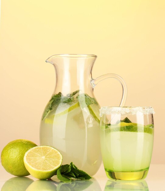 Lemonade in pitcher and glass on yellow background