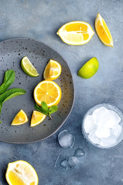 Foto preparazione della limonata in vetro con cubetti di ghiaccio ingredienti freschi limone e menta su piatto in ceramica grigia