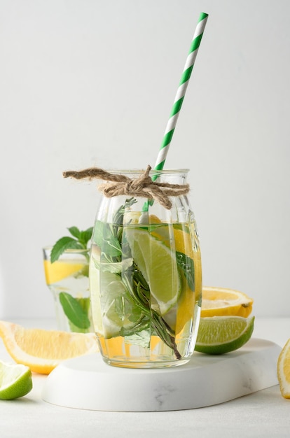 Limonata in un bicchiere trasparente con rametti di rosmarino limone lime e foglie di menta su sfondo bianco