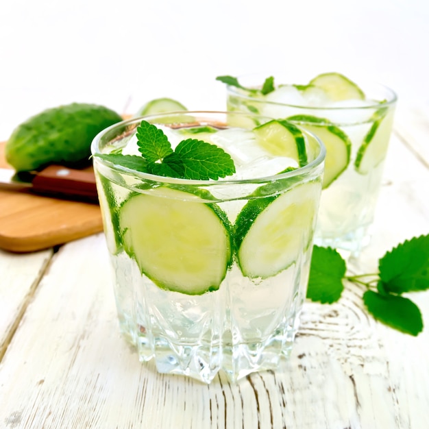 Lemonade with cucumber and mint in two glasses, a knife, a cucumber on the background light wooden boards