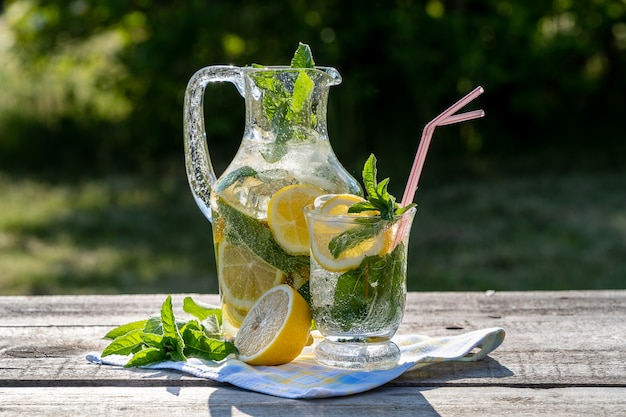 Lemonade with lemon, mint and ice, in a jug and a jar, over old wooden table, outdoor.