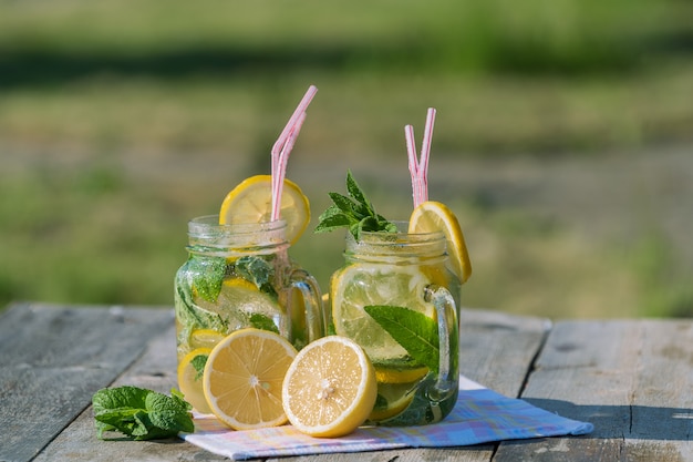 Lemonade with lemon, mint and ice, in a jug and a jar  over old wooden table