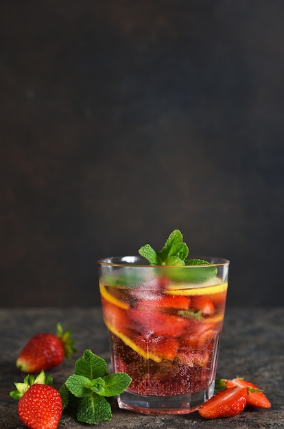 Lemonade with strawberries and mint on a dark concrete table.