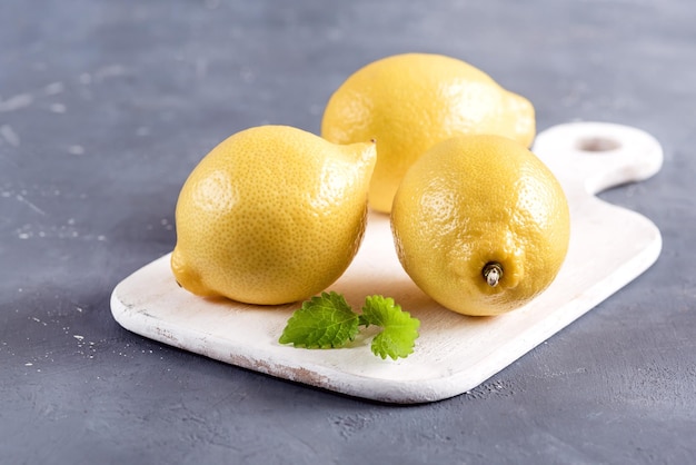 Lemons on cutting board on grey background Fresh yellow citrus Mint leaf